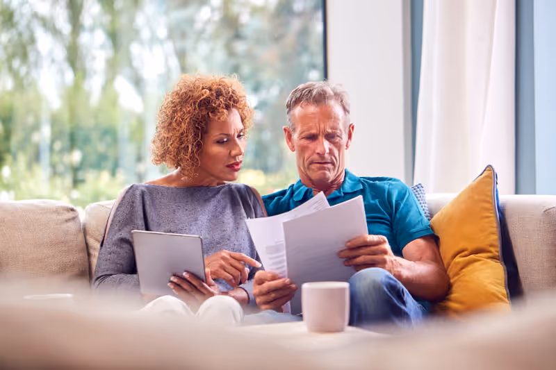 Couple sitting at a kitchen table reviewing documents together, looking relaxed and focused.