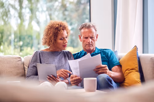 Couple sitting at a kitchen table reviewing documents together, looking relaxed and focused.